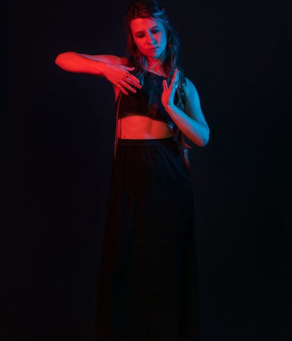 Woman performing a fluid yoga pose in a dark room with cyan highlights.